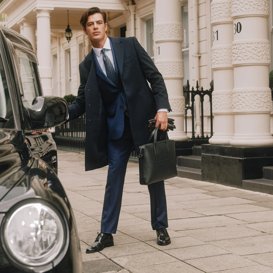 Man in Hawes and Curtis suit opening a black cab door