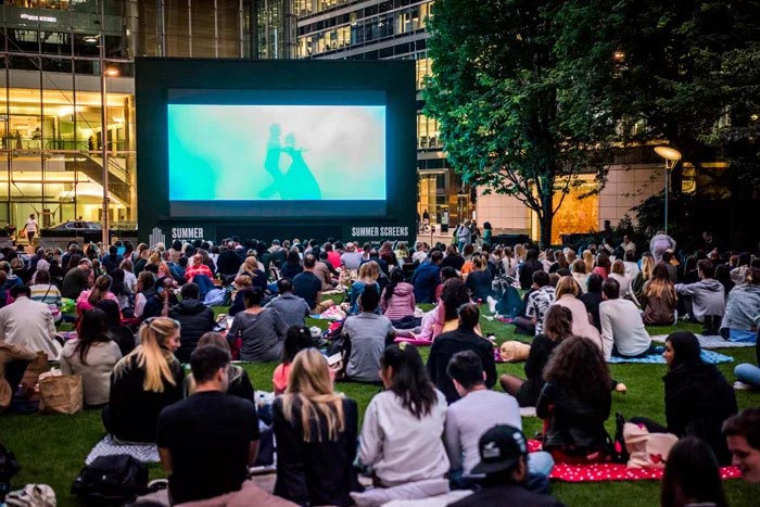 A crowd engrossed in a movie on a screen in an open lawn