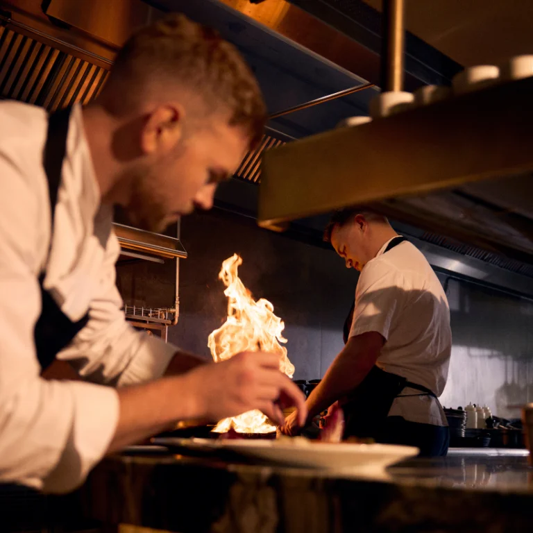 chefs plating dishes with fire cooking in background