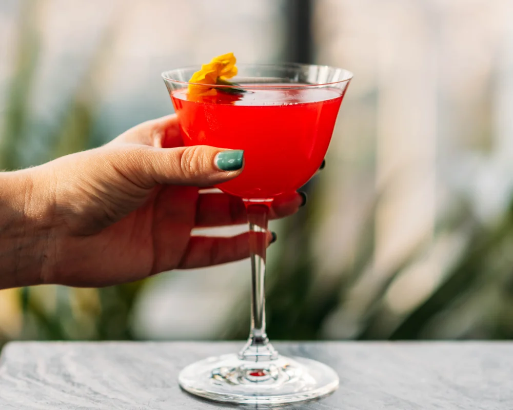 person with green nail polish holiday a red cocktail